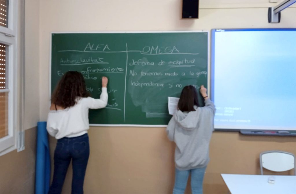 Dues alumnes escrivint a la pissarra els arguments dels bàndols Alfa i Omega en la simulació de la Guerra de Secessió