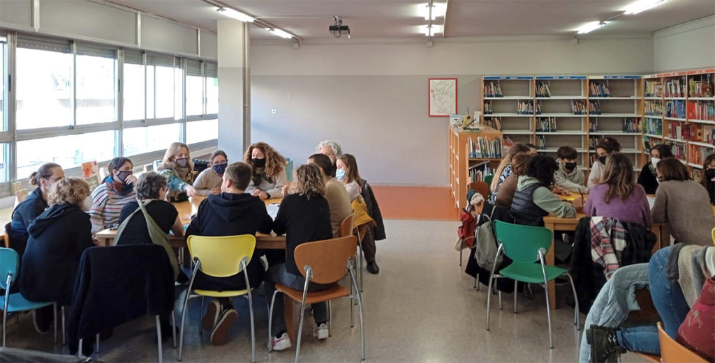 Claustre de mestres reunit en grans taules a la biblioteca de l'escola durant una sessió del projecte Harmonia a l'Aula