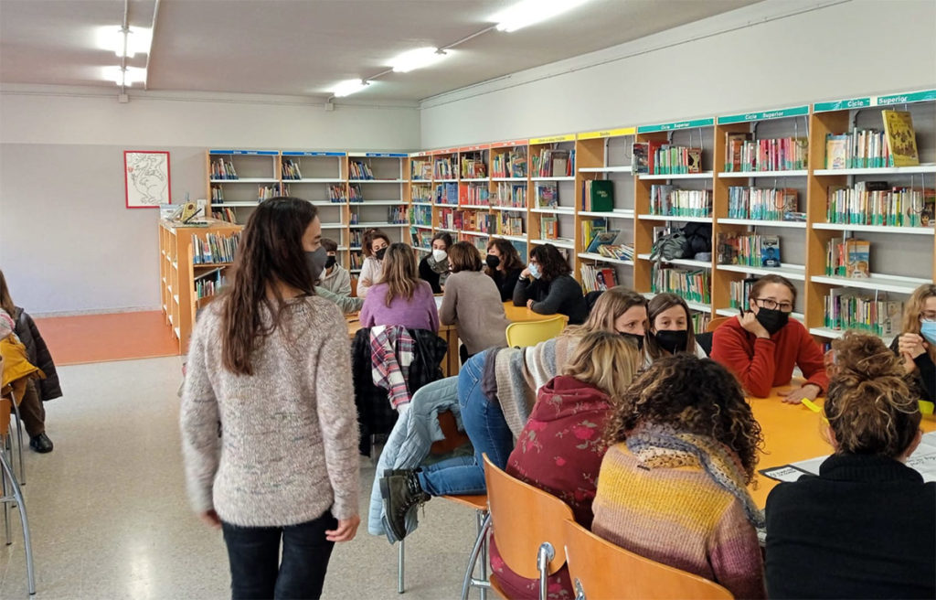 Mestres treballant en petits grups al voltant de taules de la biblioteca dins l'espai d'escolta del projecte Harmonia a l'Aula
