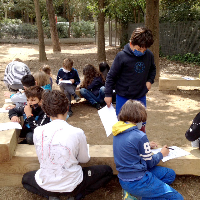 Infants treballant en grup a l'aire lliure escrivint i dibuixant durant una sessió del projecte d'art i gestió de conflictes